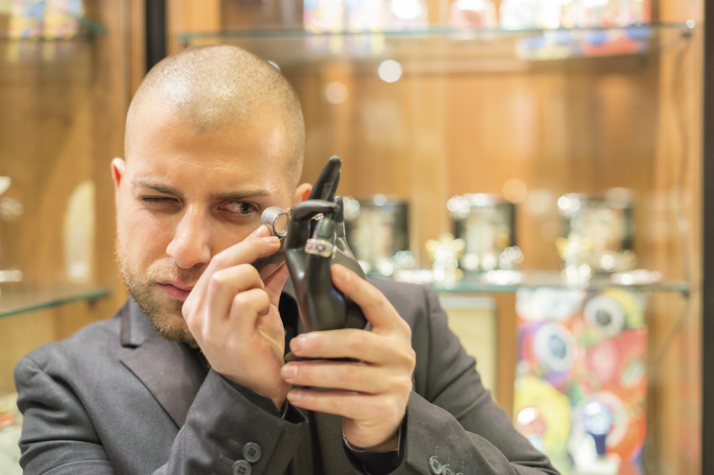 Gemologist inspecting some gem-set jewelry objects with his magnifying glass